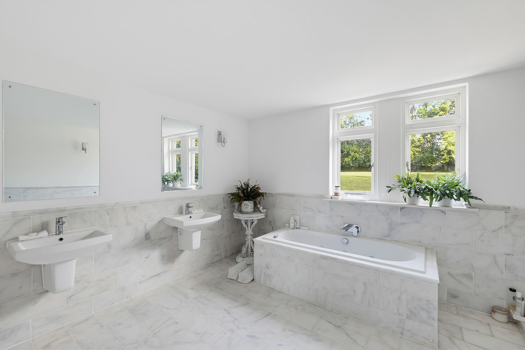 Bright bathroom with white marble-effect tiles, twin basins, a bathtub and natural window light
