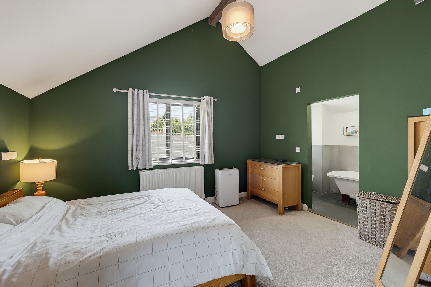 Bedroom with deep green walls, white bedding and an adjoining en-suite bathroom