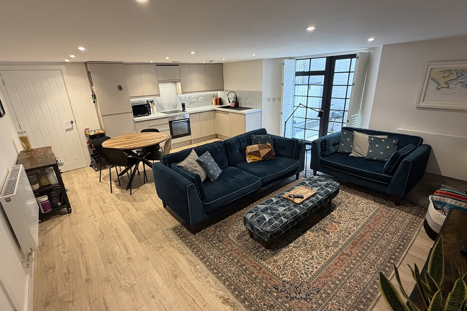 iPhone photograph of an open-plan kitchen and sitting room with blue sofas, showing a wider viewpoint and warmer lighting