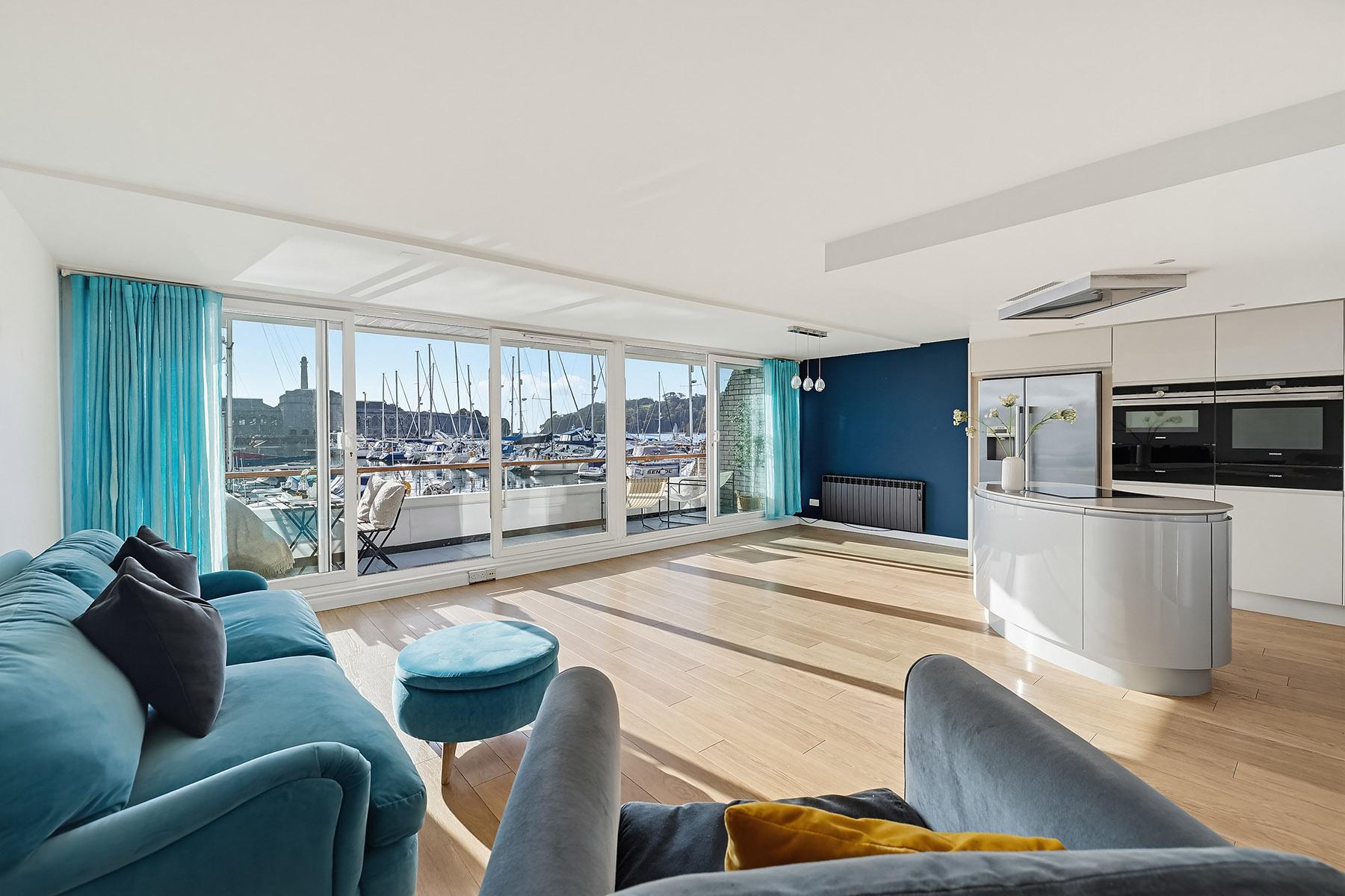 Professionally photographed open-plan waterfront apartment with balanced interior lighting, turquoise furnishings and marina views through the windows